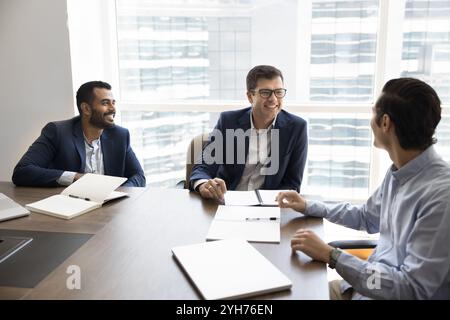 Drei verschiedene glückliche junge Geschäftsmänner treffen sich in informellen Anzügen im Büro Stockfoto