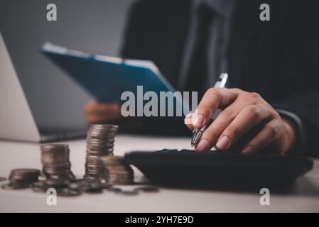 Geschäftsmann berechnet Finanzen mit Stapeln von Münzen, Zwischenablage und Rechner, wobei er die Finanzplanung und -Analyse betont. Geeignet für Finanz-, Stockfoto