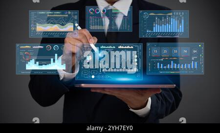 Geschäftsmann mit einem Tablet mit Eingabestift zur Analyse von Finanzdaten auf einem futuristischen digitalen Dashboard mit visuellen Analysen und Diagrammen Business Intelli Stockfoto