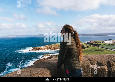 Junge Frau, die den Blick auf das Meer am Küstenaussichtspunkt am Turm des herkules bewundert Stockfoto