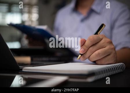 Geschäftsexperte, die sich Notizen in einem Notizbuch machen, während sie Dokumente an einem Schreibtisch prüfen, Planungsorganisation und Geschäftsstrategieentwicklung entwickeln. Unterdrücken Stockfoto