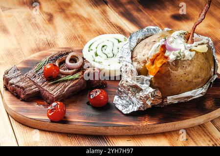 Rindfleisch, Steak mit Tomaten und in Folie gebackene Kartoffeln mit Hüttenkäse und Speckchips auf hölzernem Hintergrund. Hochwertige Fotos Stockfoto