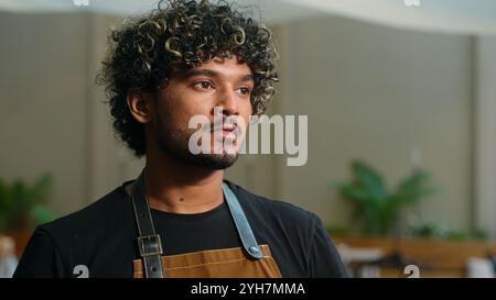 Glücklich lächelnd fröhlich junger indischer arabischer Mann Cafe Arbeiter in Schürze männlicher Mann Kellner Cleaner Blick Distanz denken drehend Blick auf Kamera freundlich Stockfoto