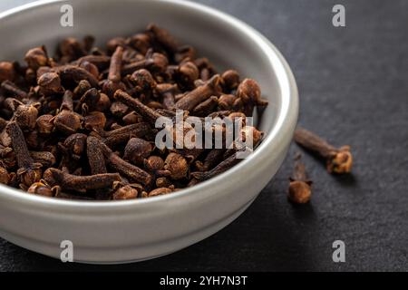 Ganze Nelken würzen in einer Schüssel auf schwarzem Hintergrund. Trockene Nelkenknospen in einer grauen Keramikschale. Kochen, Kräutermedizin und Gewürzkonzept. Nahaufnahme. Stockfoto