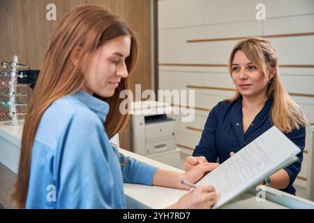 Weibliche Erwachsene Patientin, die Dokumente mit der Empfangsdame überprüft Stockfoto