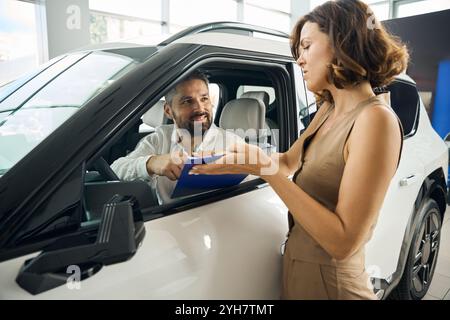 Ein lächelnder Mann, der Dokumente unterschreibt, während er im neuen Auto sitzt Stockfoto