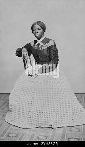 Eine Carte-de-Visite von Harriet Tubman (ca. 46-47) in den Jahren 1868-69. Sie sitzt, nach links gedreht. Eine Hand liegt auf der Rückseite eines Holzstuhls, eine andere auf ihrem Schoß. Erstellt von Benjamin Powelson, 77 Genesee St., Auburn, New York. Harriet Tubman saß in einem Innenraum. Sie ist leicht nach rechts gedreht und blickt von der Kamera ab. Ihre rechte Hand liegt auf der Rückseite eines Holzstuhls und ihre linke Hand auf ihrem Schoß. Ein kühn gemusterter Teppich bedeckt den Boden und die Wand oder fällt hinter ihr in einer leeren hellen Farbe. Tubman trägt ein schwarzes Mieder, das vorne in der Mitte Knöpfe und Stockfoto