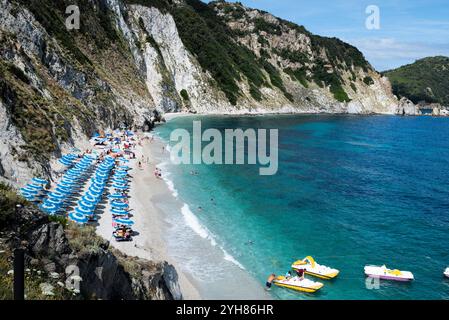 Sansone Strand auf der Insel Elba im Sommer, mit Liegestühlen und Sonnenschirm mit vielen Badegästen am Meer und bunten Paddelbooten Stockfoto