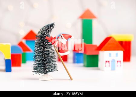 Plastilin Santa Claus versucht, einen Stern an einen Weihnachtsbaum zu hängen, vor einem verschwommenen Hintergrund eines Dorfes aus Holzblöcken. Weihnachten und New Yea Stockfoto