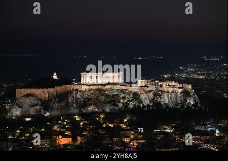 Blick auf die Stadt Athen und den Akropolis-Hügel mit dem Parthenon-Tempel, der nach Sonnenuntergang über dem Saronischen Golf beleuchtet wird. Athen, Griechenland Stockfoto