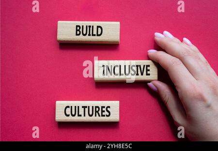 Symbol „integrative Kulturen erstellen“. Holzblöcke mit Wörtern bilden inklusiv-Kulturen. Schöner roter Hintergrund. Geschäftsmann Hand. Business and Build Inc Stockfoto