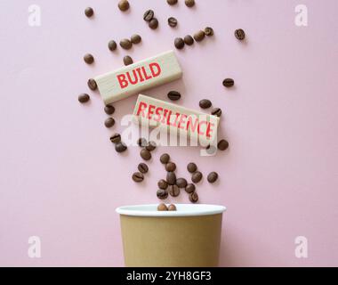 Symbol für Belastbarkeit erstellen. Holzklötze mit Wörtern sorgen für Widerstandsfähigkeit. Schöner rosafarbener Hintergrund mit Kaffeetasse. Business- und Build Resilience-Konzept. Stockfoto