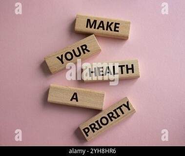 Gesundheitssymbol. Holzblöcke mit Worten machen Ihre Gesundheit zu einer Priorität. Schöner rosafarbener Hintergrund. Gesundheitskonzept. Kopierbereich. Stockfoto