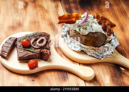 Gebratenes Rindfleisch mit Tomaten und Kartoffeln, gebacken in Folie mit Hüttenkäse und Speckchips auf hölzernem Hintergrund. Hochwertige Fotos Stockfoto