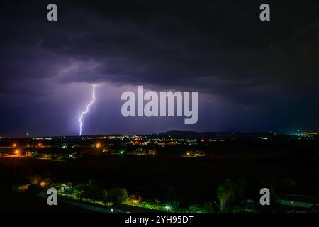 Ein brillanter Blitz beleuchtet die dunklen Wolken über einer ruhigen Landschaft am Abend. Stockfoto