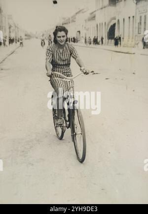 Subotica, Jugoslawien - 1940: Yong-Frau in gestreiftem Kleid, die auf der Straße Fahrrad fährt Stockfoto