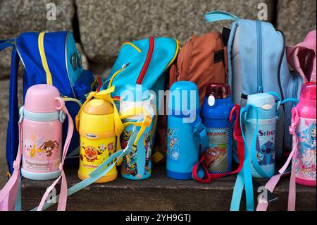 Kindergartenschule Kinderrucksäcke und Thermosflaschen auf einer Bank bilden ein farbenfrohes Stillleben der japanischen Kultur. Stockfoto