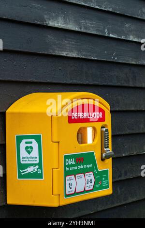 Defibrillator in gelber, gut sichtbarer Box an der Außenseite eines Gebäudes an einem öffentlichen Ort für den Einsatz im kardialen Notfall. Stockfoto