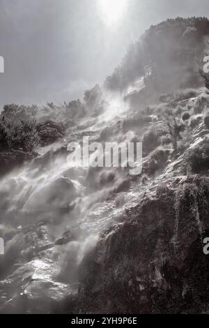 Ein dramatisches Schwarzweiß-Bild, das einen nebeligen Wasserfall einfängt, der eine felsige Klippe hinunterstürzt. Stockfoto