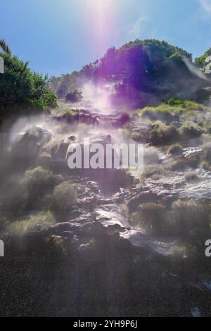 Eine mystische Szene, in der Nebel von den felsigen Hängen eines Wasserfalls aufsteigt. Das Sonnenlicht zieht durch die Bäume und strahlt ein sanftes, traumhaftes Licht auf die Landschaft Stockfoto