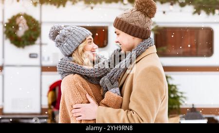 Das junge Paar zieht sich bei Schneefall an einem festlichen Ort in Winterkleidung um Stockfoto