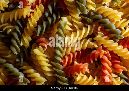 Ungekochte Fusilli Pasta in leuchtenden Farben: Eine faszinierende kulinarische Leinwand aus bunten Spiralen, die einen lebendigen und strukturierten Hintergrund für Gourmet-Kochen schafft. Farbige Trockene Pasta. Rohe Makkaroni Stockfoto