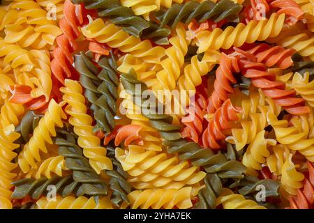 Ungekochte Fusilli Pasta in leuchtenden Farben: Eine faszinierende kulinarische Leinwand aus bunten Spiralen, die einen lebendigen und strukturierten Hintergrund für Gourmet-Kochen schafft. Farbige Trockene Pasta. Rohe Makkaroni Stockfoto