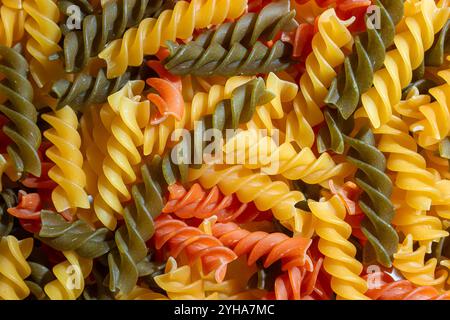 Ungekochte Fusilli Pasta in leuchtenden Farben: Eine faszinierende kulinarische Leinwand aus bunten Spiralen, die einen lebendigen und strukturierten Hintergrund für Gourmet-Kochen schafft. Farbige Trockene Pasta. Rohe Makkaroni Stockfoto