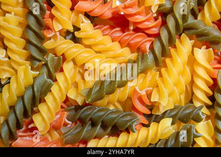 Ungekochte Fusilli Pasta in leuchtenden Farben: Eine faszinierende kulinarische Leinwand aus bunten Spiralen, die einen lebendigen und strukturierten Hintergrund für Gourmet-Kochen schafft. Farbige Trockene Pasta. Rohe Makkaroni Stockfoto