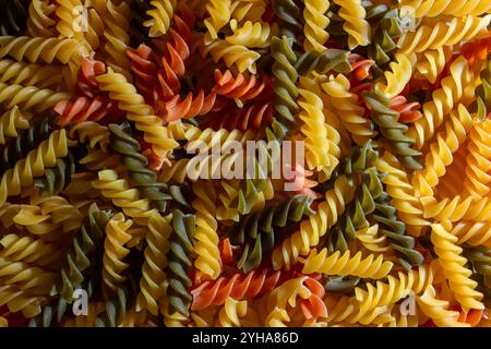 Ungekochte Fusilli Pasta in leuchtenden Farben: Eine faszinierende kulinarische Leinwand aus bunten Spiralen, die einen lebendigen und strukturierten Hintergrund für Gourmet-Kochen schafft. Farbige Trockene Pasta. Rohe Makkaroni Stockfoto