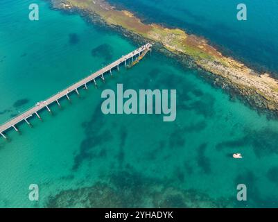 Aus der Vogelperspektive auf einen langen Küstensteg, der zu einem felsigen Riff in einer flachen Bucht bei Port Noarlunga in South Australia führt Stockfoto