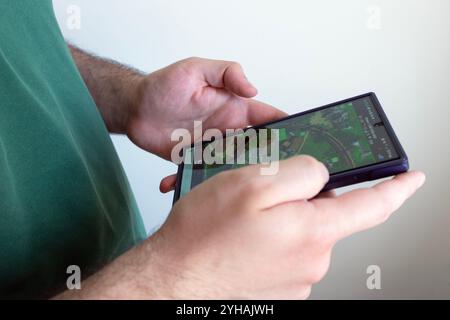 Mann, der ein Echtzeit-Strategie-Massiv-Multiplayer-Online-Spiel auf seinem Handy aus nächster Nähe spielt, trägt ein grünes T-Shirt Stockfoto