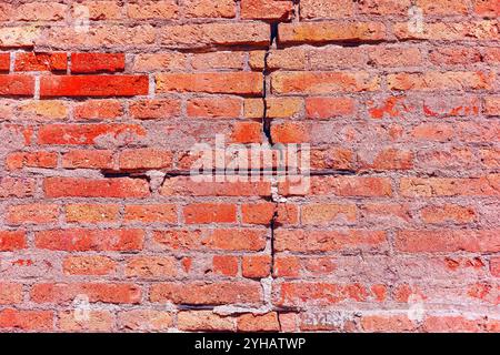 Textur der Ziegelwand, kann als Hintergrund verwendet werden. Ziegelstruktur mit Kratzern und Rissen. Ziegelwand mit deutlichem Riss, der durch die Wand verläuft Stockfoto