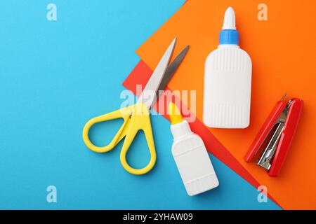 Klebstoff, buntes Papier, Hefter und Schere auf hellblauem Hintergrund, flach. Leerzeichen für Text Stockfoto