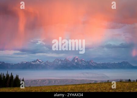 Der Sonnenaufgang erleuchtet einen Regenschauer über einem verrauchten Jackson Hole, Wyoming und Teton Mountains aus dem Red Rock Fire von 2011. Stockfoto