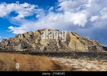 Dramatische Sandsteinklippen erheben sich über trockenem Savannengras unter hellblauem Himmel mit verstreuten weißen Wolken. Jurassische geologische Formationen A Stockfoto