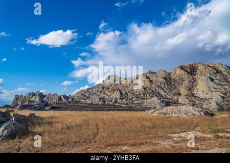 Dramatische Sandsteinklippen erheben sich über trockenem Savannengras unter hellblauem Himmel mit verstreuten weißen Wolken. Jurassische geologische Formationen A Stockfoto