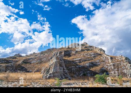 Dramatische Sandsteinklippen erheben sich über trockenem Savannengras unter hellblauem Himmel mit verstreuten weißen Wolken. Jurassische geologische Formationen A Stockfoto