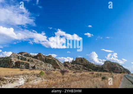 Dramatische Sandsteinklippen erheben sich über trockenem Savannengras unter hellblauem Himmel mit verstreuten weißen Wolken. Jurassische geologische Formationen A Stockfoto