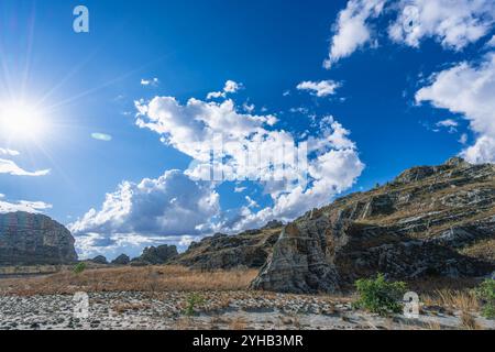 Dramatische Sandsteinklippen erheben sich über trockenem Savannengras unter hellblauem Himmel mit verstreuten weißen Wolken. Jurassische geologische Formationen A Stockfoto