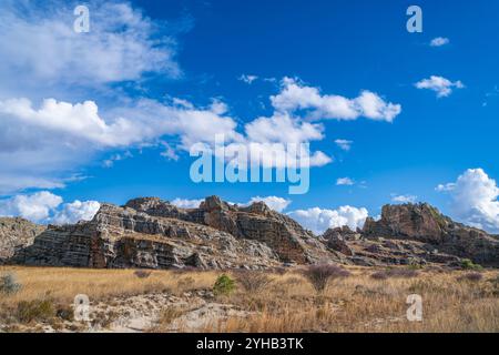 Dramatische Sandsteinklippen erheben sich über trockenem Savannengras unter hellblauem Himmel mit verstreuten weißen Wolken. Jurassische geologische Formationen A Stockfoto