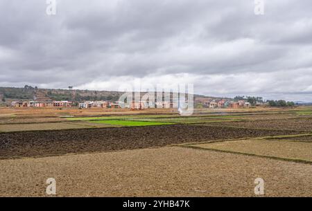 Eine ruhige ländliche Szene in Madagaskar mit grünen und braunen Terrassenfeldern. Ein weit entferntes Dorf ist eingebettet zwischen sanften Hügeln. Das Bild Stockfoto