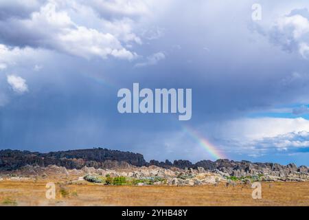 Ein lebhafter Regenbogenbogen überzieht die zerklüftete Landschaft des Isalo National Park. Dramatische Wolken verbessern die Szene. Isalo Nationalpark, Madagaskar. Stockfoto