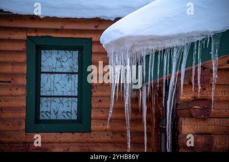 Hängende lange Eiszapfen auf der Seite einer atemberaubenden Blockhütte, Haus, Hausgebäude mit scharfen Kanten im Winter. Stockfoto