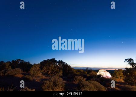 Ein Zelt, das im letzten Licht des Tages von innen beleuchtet wird, auf dem Campingplatz im Dead Horse Point State Park in der Nähe von Moab, Utah Stockfoto