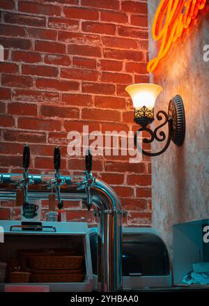 Café-Inneneinrichtung im Vintage-Stil mit leuchtender Wandleuchte, freiliegender Ziegelwand und Bierhähnen für eine gemütliche und einladende Atmosphäre Stockfoto