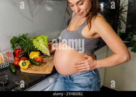 Glückliche schwangere Frau, die zu Hause kocht und frischen grünen Salat macht Stockfoto
