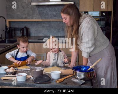 Mutter und ihre Kinder bereiten in einer modernen Küche gerne Keksenteig zu, während sie über das Backen kleben. Die Familie genießt eine gute Zeit zusammen, lernen und Stockfoto