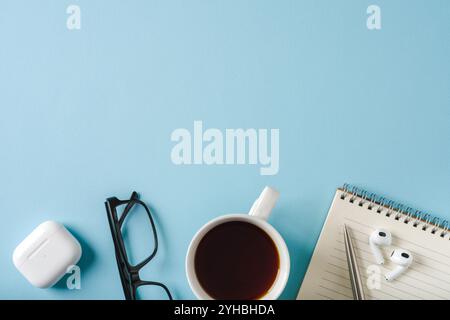 Ansicht von oben auf Notebook, Gläser, Kaffee, Kopfhörer und Kugelschreiber auf blauem Hintergrund Stockfoto