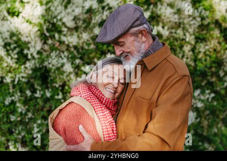 Porträt eines schönen Seniorenpaares draußen in einem Herbstgarten. Ältere Ehemann und Ehefrau umarmen sich gegenseitig. Stockfoto